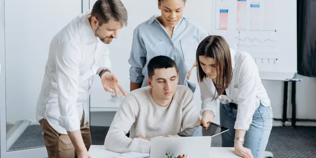 Groupe d’apprenants travaillant en équipe autour d’un ordinateur portable, analysant des documents et des graphiques dans une salle de formation.