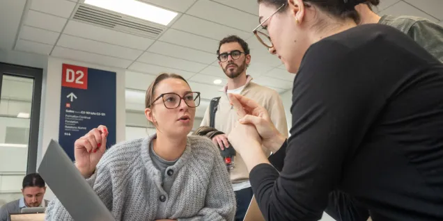 Groupe de personnes travaillant ensemble autour d’une table avec des ordinateurs portables dans un espace intérieur lumineux, en échangeant des informations et des documents.