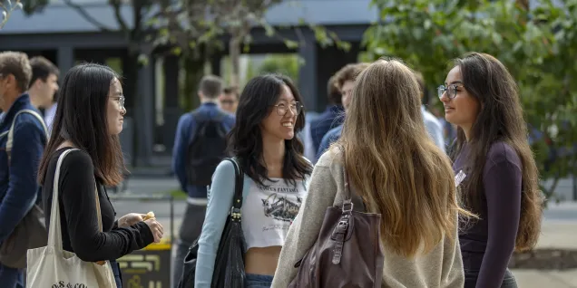 Group of emlyon students talking outdoors on campus, surrounded by other people and trees.
