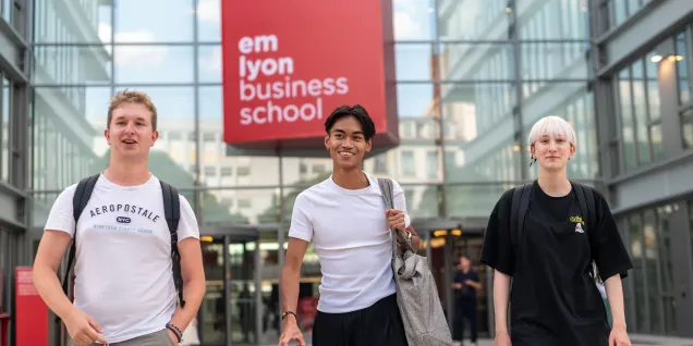 Étudiants marchant devant l’entrée d'emlyon business school sur le campus, devant le bâtiment principal au logo rouge.