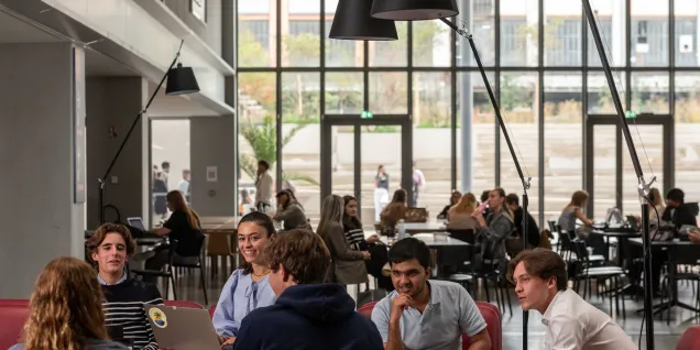 Étudiants d’emlyon business school travaillant et échangeant dans un espace commun du campus, avec vue sur l’atrium et les tables de travail.