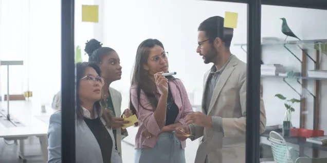 Team collaborating around a glass board, sharing ideas and working with sticky notes in a modern office workspace.