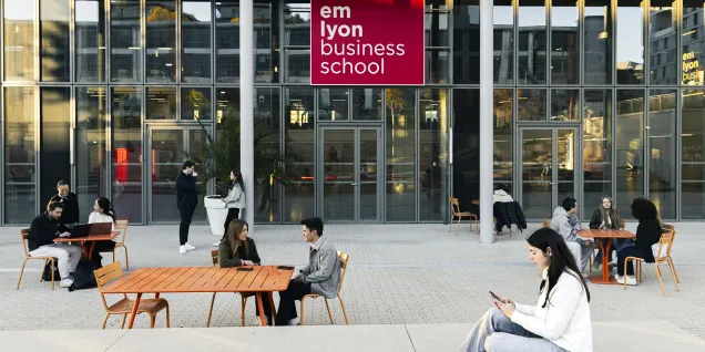 Étudiants assis et échangeant sur la terrasse extérieure du campus emlyon business school.