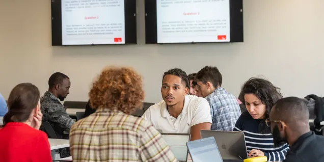 Groupe d’étudiantes et étudiants d'emlyon business school collaborant en classe devant des écrans affichant une présentation pédagogique.
