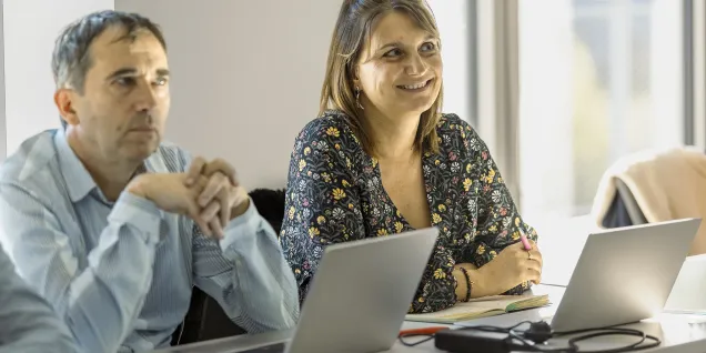 emlyon participants attending a training session, seated at a table with laptops, taking notes and working in a bright classroom setting.