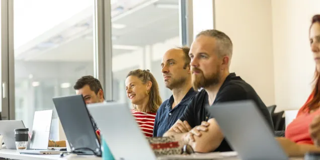 Participants in the E2MG program at emlyon business school attending a class and working on laptops in a bright classroom.