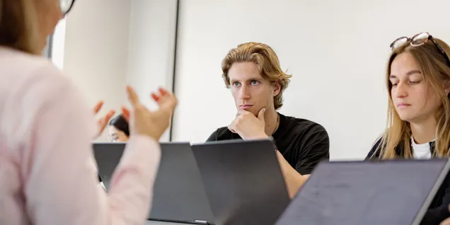 emlyon students working together on laptops during a collaborative study session in a classroom.