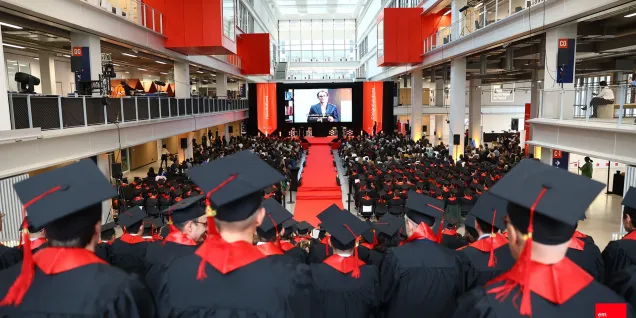 Vue panoramique de la cérémonie de remise des diplômes d’emlyon business school dans l’atrium, avec les diplômés assis face à la scène.