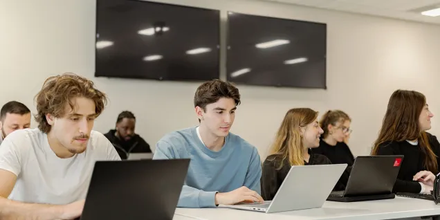 Executive MBA participants attending a class at emlyon, seated at desks and working on laptops in a modern learning environment.