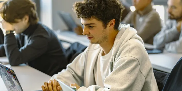 Students seated in a classroom, working on laptops during a class session.