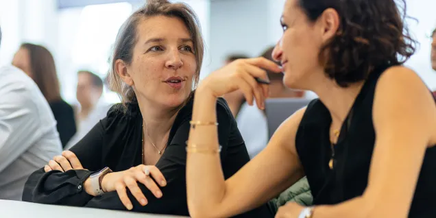 Deux personnes discutent à une table pendant une session de travail en groupe dans une salle de formation.