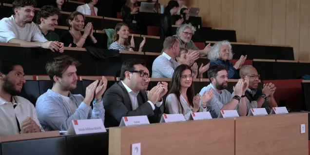 Public assis dans un amphithéâtre universitaire, applaudissant après une présentation ou une conférence.