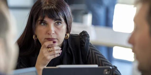 Person attending a business meeting, seated in front of a tablet and interacting with colleagues in a professional workplace setting.