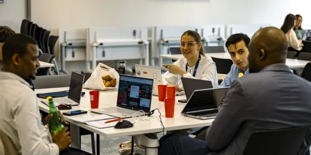 Groupe de collaborateurs travaillant sur ordinateurs portables autour d’une table lors d’un atelier en salle de formation