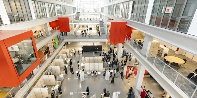 Atrium lumineux d’un campus avec espaces de travail, stands et visiteurs répartis sur plusieurs niveaux