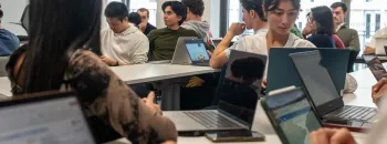 “IMBA students at emlyon working together in a bright classroom, seated around tables with laptops, engaged in discussion and collaborative work.