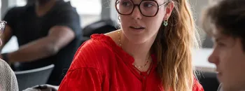 Student in a classroom working on a laptop during an in‑person lesson, in a bright room with large windows.