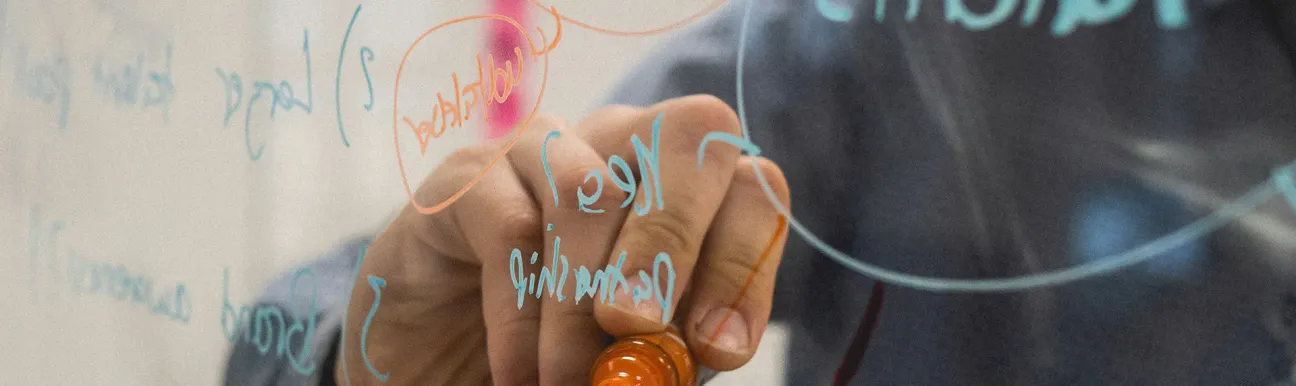A man's hand holding a marker and writing on a transparent whiteboard