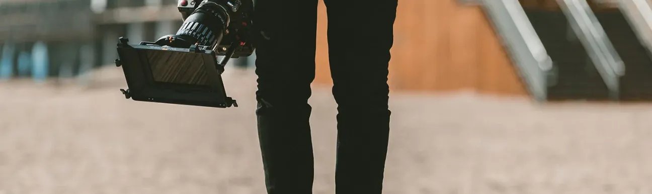 A person standing, of whom we see only one half, holding a professional camera in their right hand.
