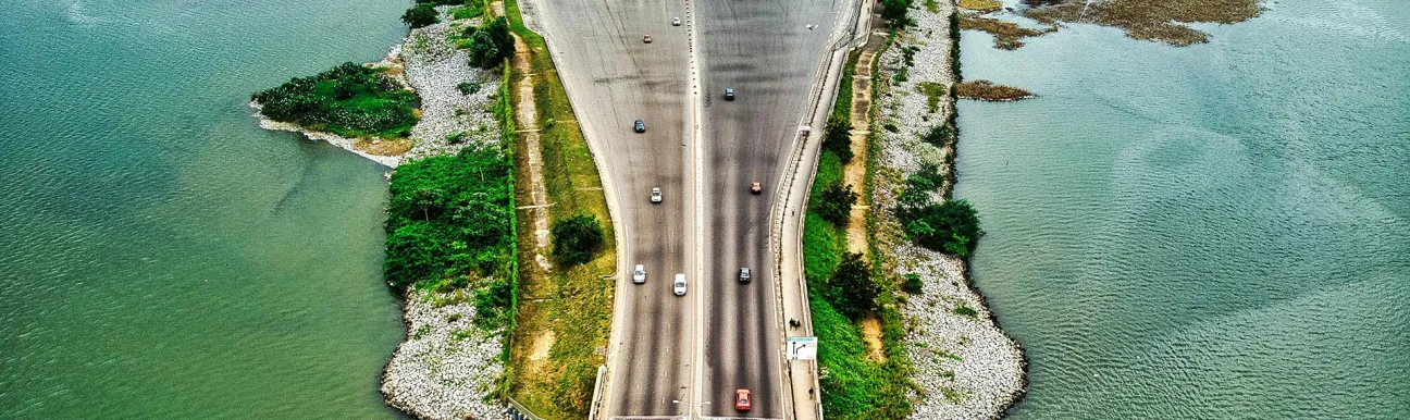 Vue aérienne d’un pont routier à plusieurs voies traversant une lagune à Abidjan, avec un péage, des véhicules en circulation et des berges végétalisées.