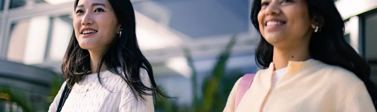 Deux personnes marchant dans un espace extérieur moderne, devant un bâtiment contemporain, dans un contexte académique ou professionnel.