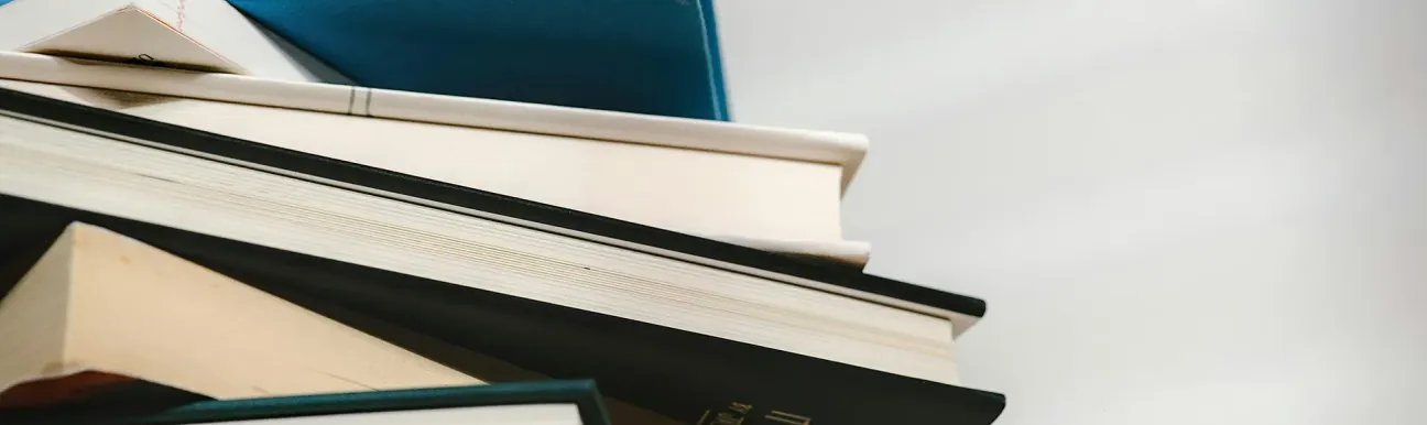 Pile de plusieurs livres reliés de différentes couleurs, empilés en biais, sur un fond clair.