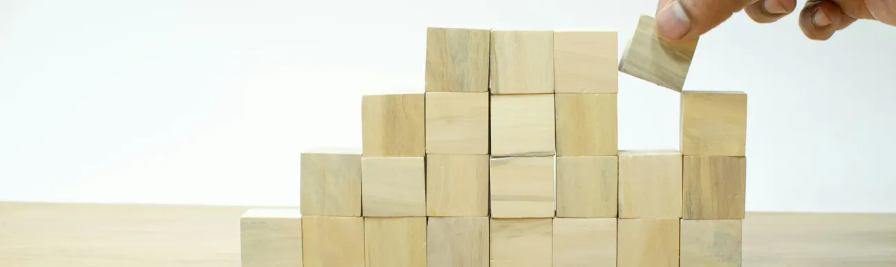 Main plaçant un bloc en bois au sommet d’une structure de cubes en bois disposés en escalier sur une table.