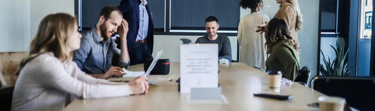 Plusieurs personnes réunies autour d’une grande table dans une salle de réunion, avec ordinateurs portables et documents.