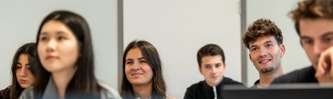 Un groupe de personnes assises dans une salle de classe utilise des ordinateurs portables, avec une porte fermée visible au fond de la pièce.