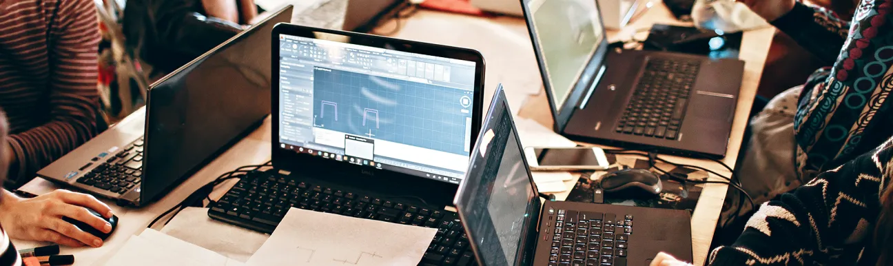 Group of people using laptops and reviewing technical plans and diagrams during a collaborative work session in a tech environment