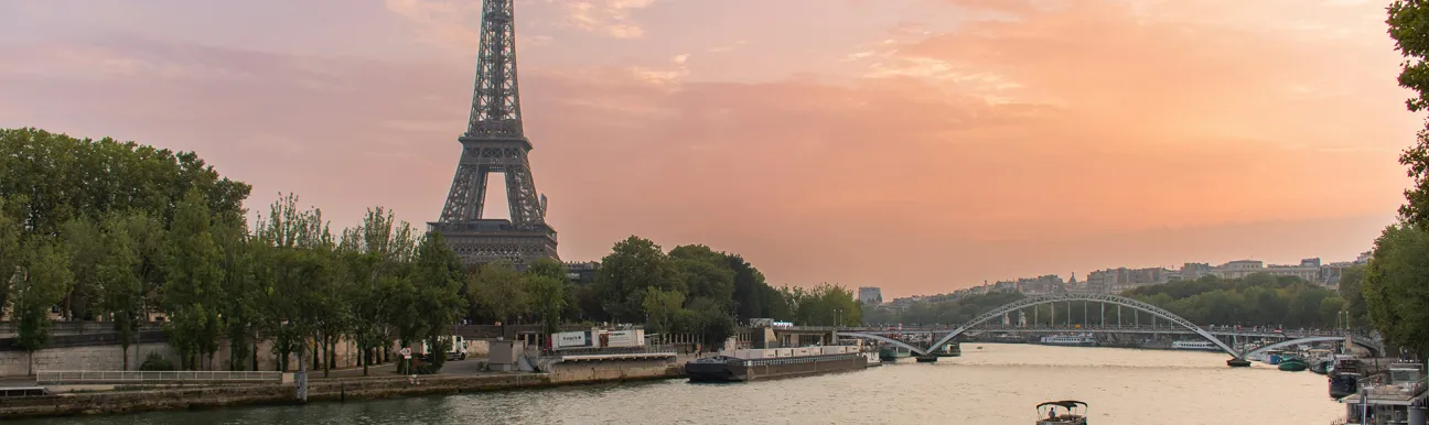 View of the Eiffel Tower and the Seine River at sunset with a boat sailing through Paris.