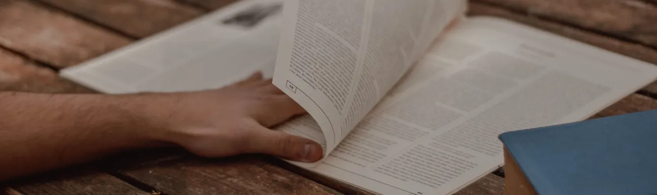 Personne feuilletant une revue académique sur une table en bois, avec un livre relié à proximité. Afficher plus de lignes