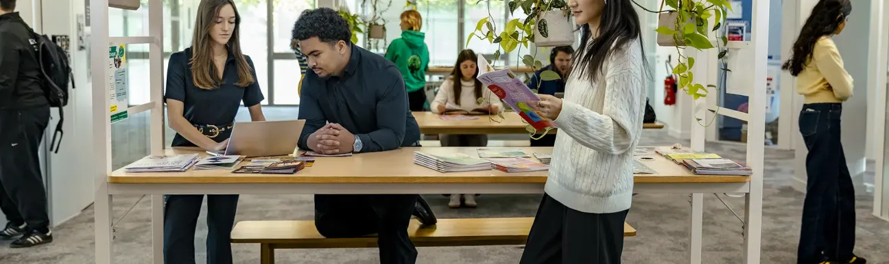 Personnes consultant des brochures et un ordinateur autour d’une table dans un espace intérieur végétalisé.