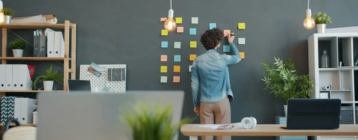 A person, seen from behind, writing on a whiteboard inside an office.