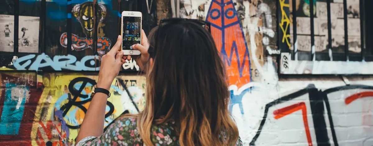 A young woman captures the essence of a graffiti-covered wall with her smartphone.