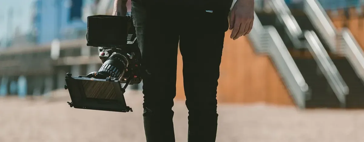 A person standing, of whom we see only one half, holding a professional camera in their right hand.
