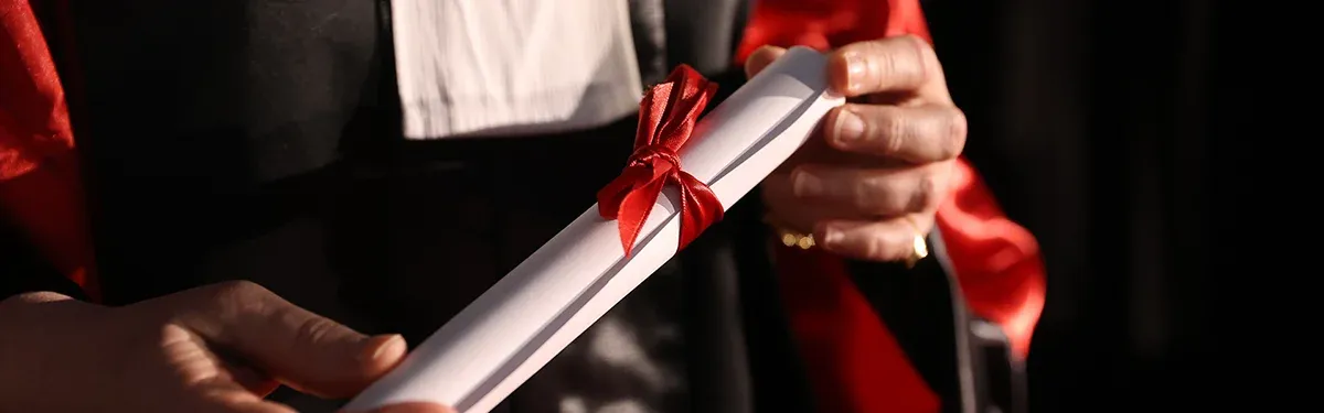 Main tenant un diplôme roulé avec un ruban rouge lors d’une cérémonie de remise de diplômes.