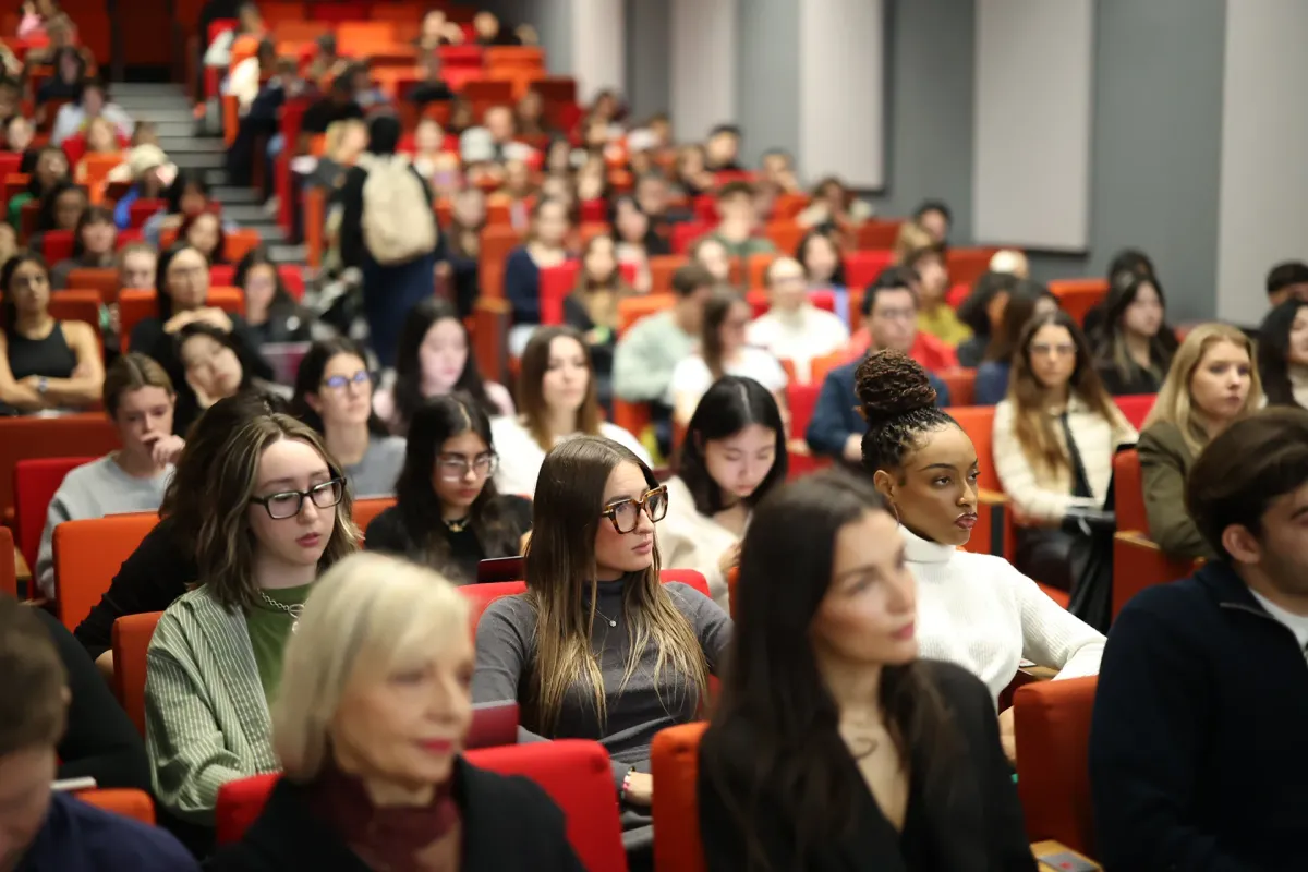 View of an amphitheater at the emlyon Paris campus with many students seated in red chairs, attending a class or lecture.