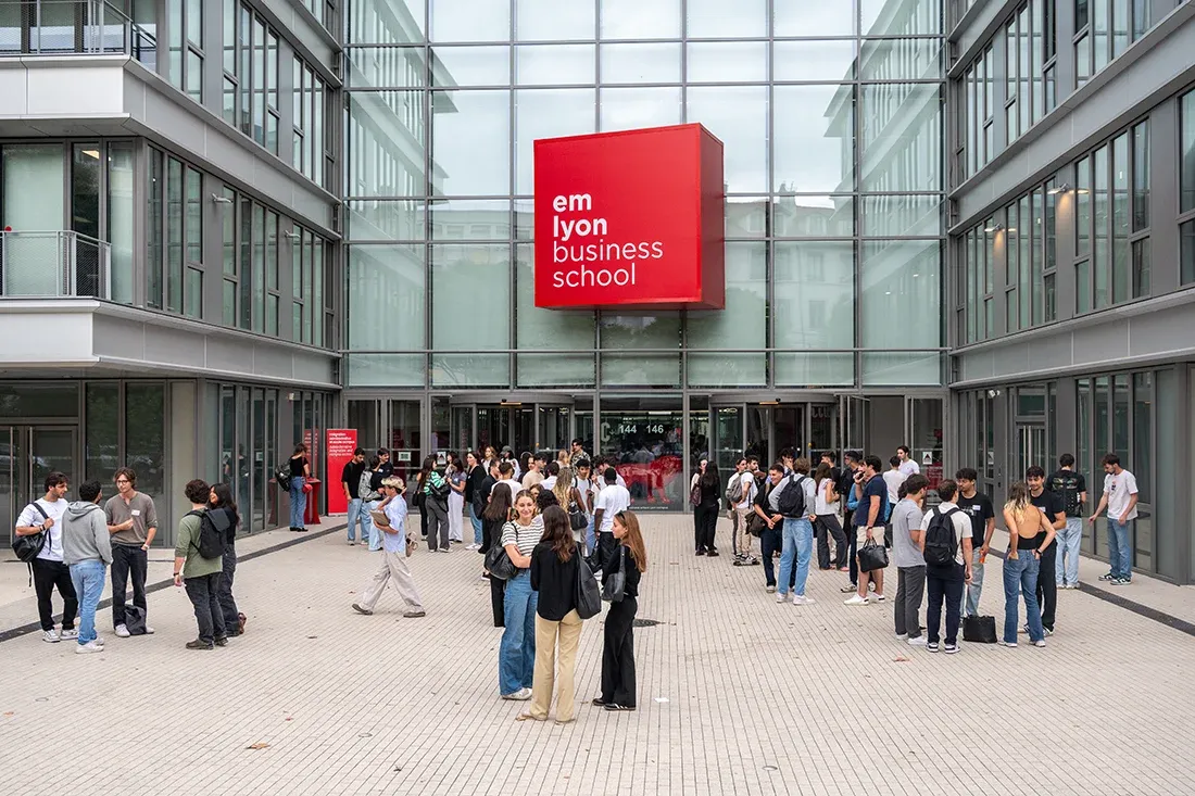 emlyon business school students gathered outside on the Lyon campus forecourt in front of the main entrance.