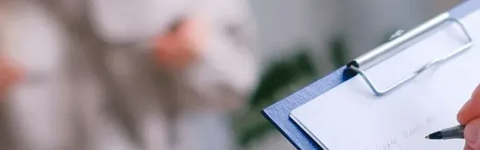Main écrivant sur un clipboard lors d’un entretien professionnel, symbole d’accompagnement et de suivi dans le secteur santé‑prévoyance.