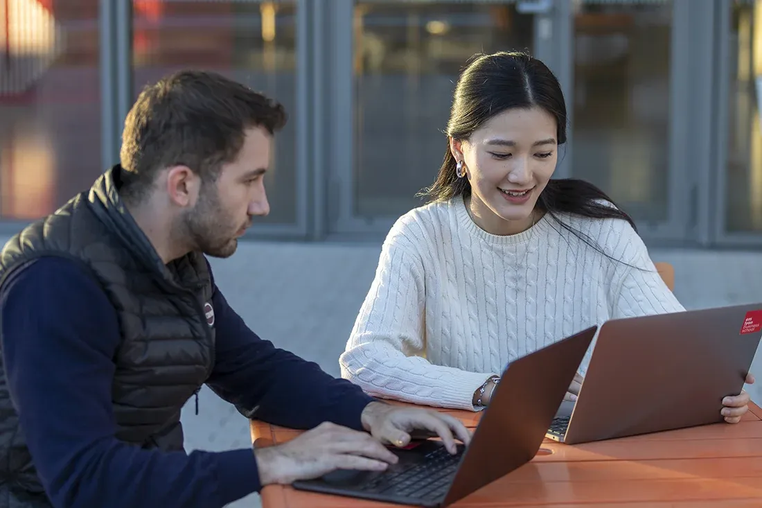 Deux étudiants emlyon travaillant ensemble sur des ordinateurs portables en extérieur sur le campus 