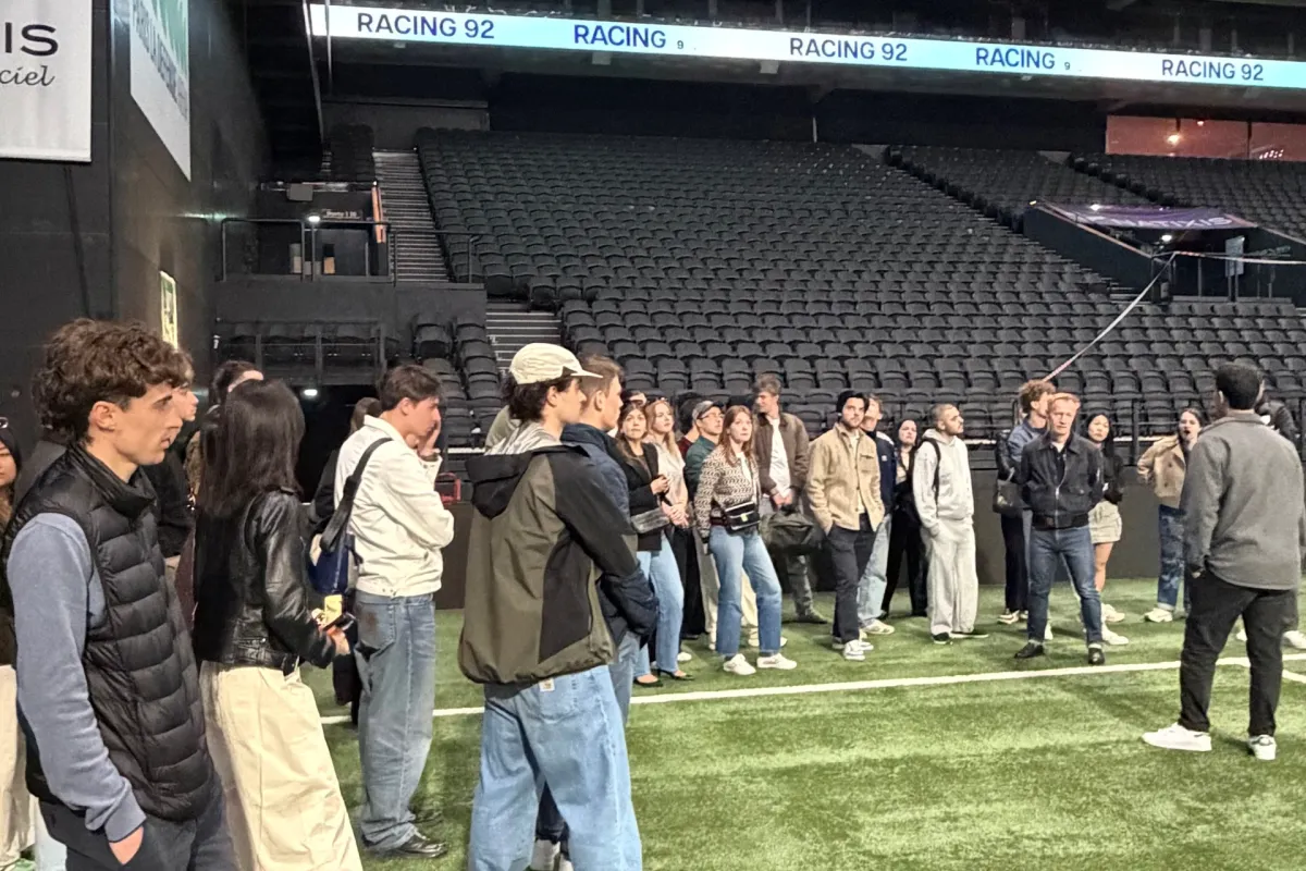  Guided tour group standing on the field of a large stadium, observing the Racing 92 facilities and seating areas.
