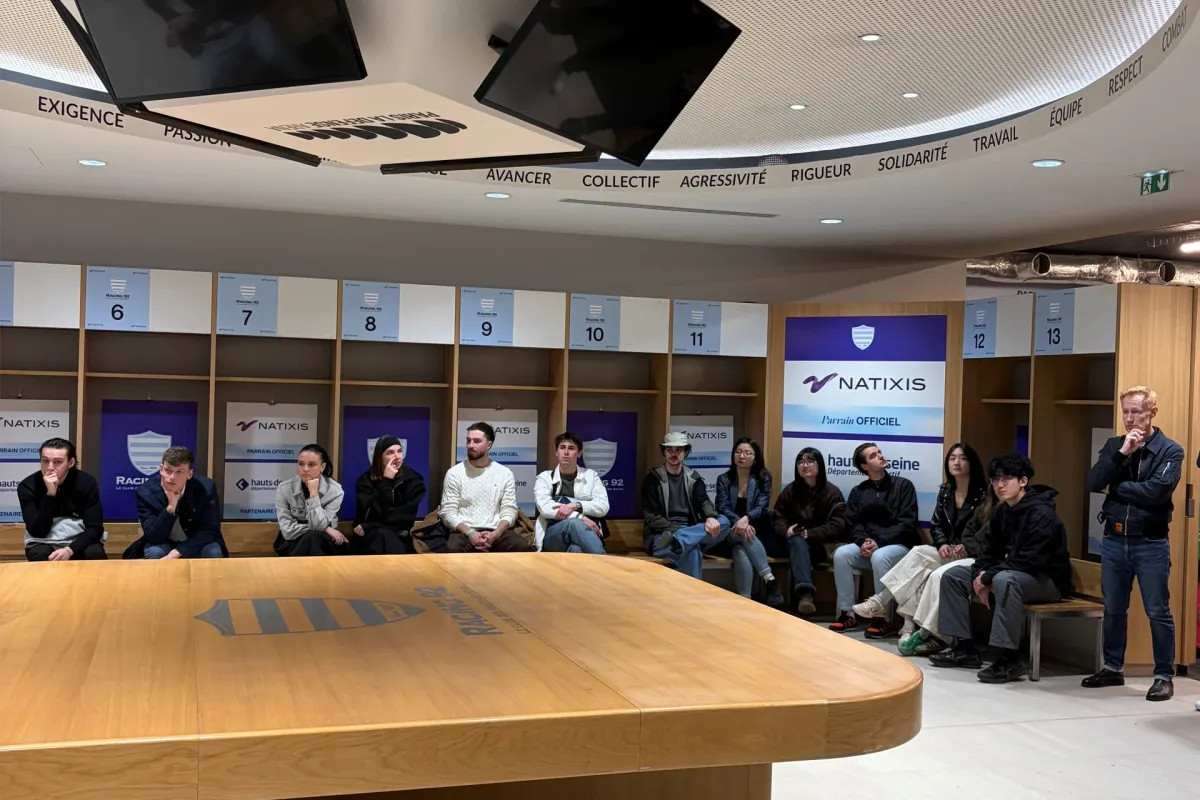 Guided tour group standing on the field of a large stadium, observing the Racing 92 facilities and seating areas.
