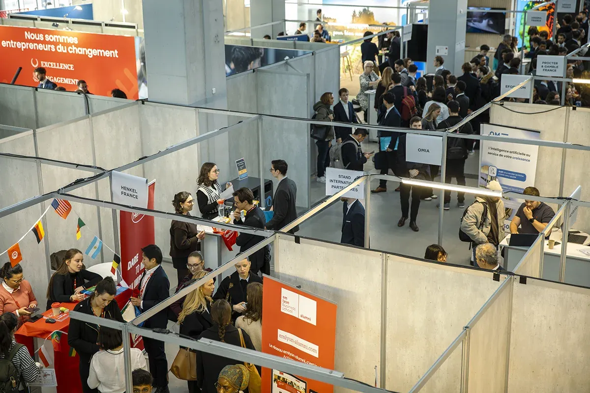 Vue d’ensemble du forum carrières d'emlyon en intérieur, avec de nombreux stands et des personnes échangeant dans un espace d’exposition.