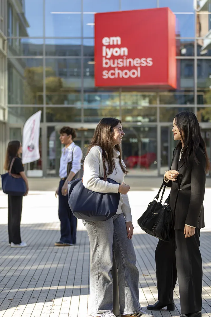 People talking outdoors in front of the emlyon business school building, visible in the background.