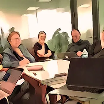 Groupe de personnes assises autour d’une table lors d’une réunion, avec un ordinateur portable ouvert au premier plan.