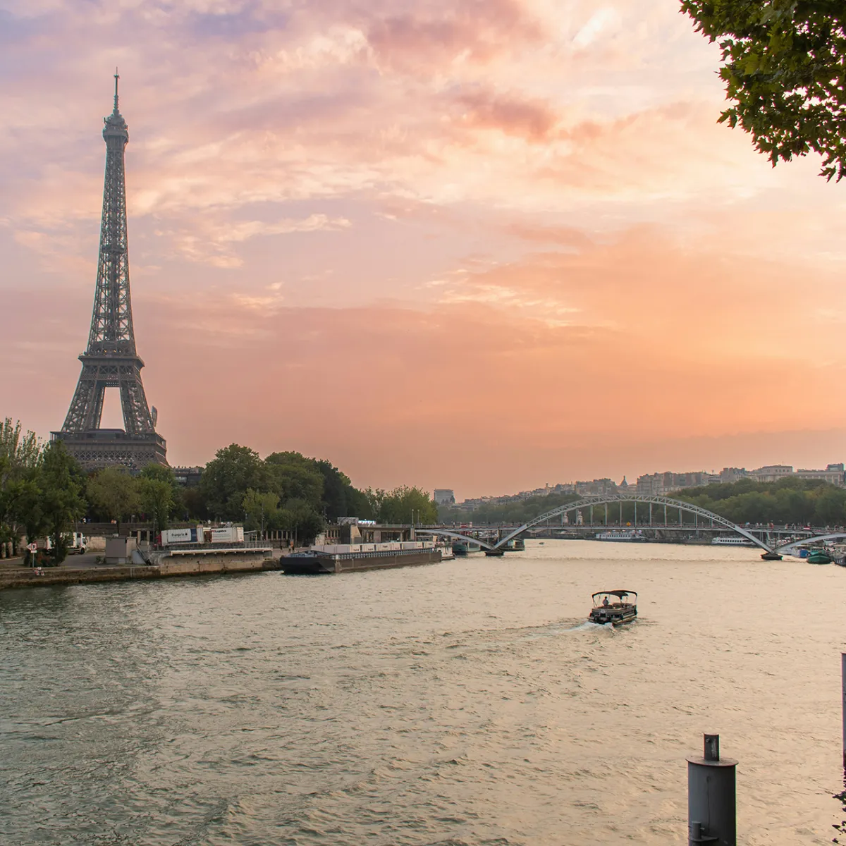 View of the Eiffel Tower and the Seine River at sunset with a boat sailing through Paris.