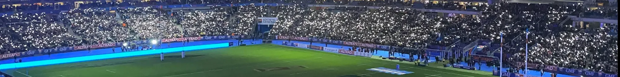 Vue du terrain de rugby avec des lumières scintillantes dans un stade rempli de supporters.