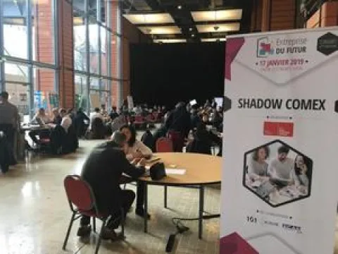 Une grande salle avec des personnes assises à des tables, discutant et interagissant dans un environnement convivial.