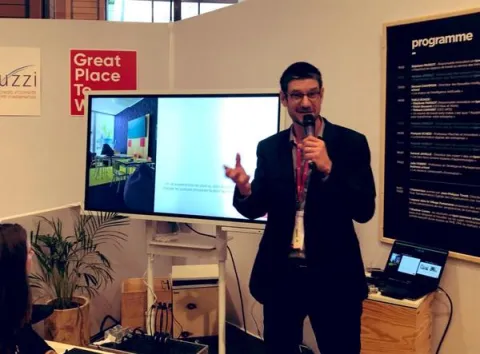 Un homme en costume s'adresse à l'audience lors d'une conférence.